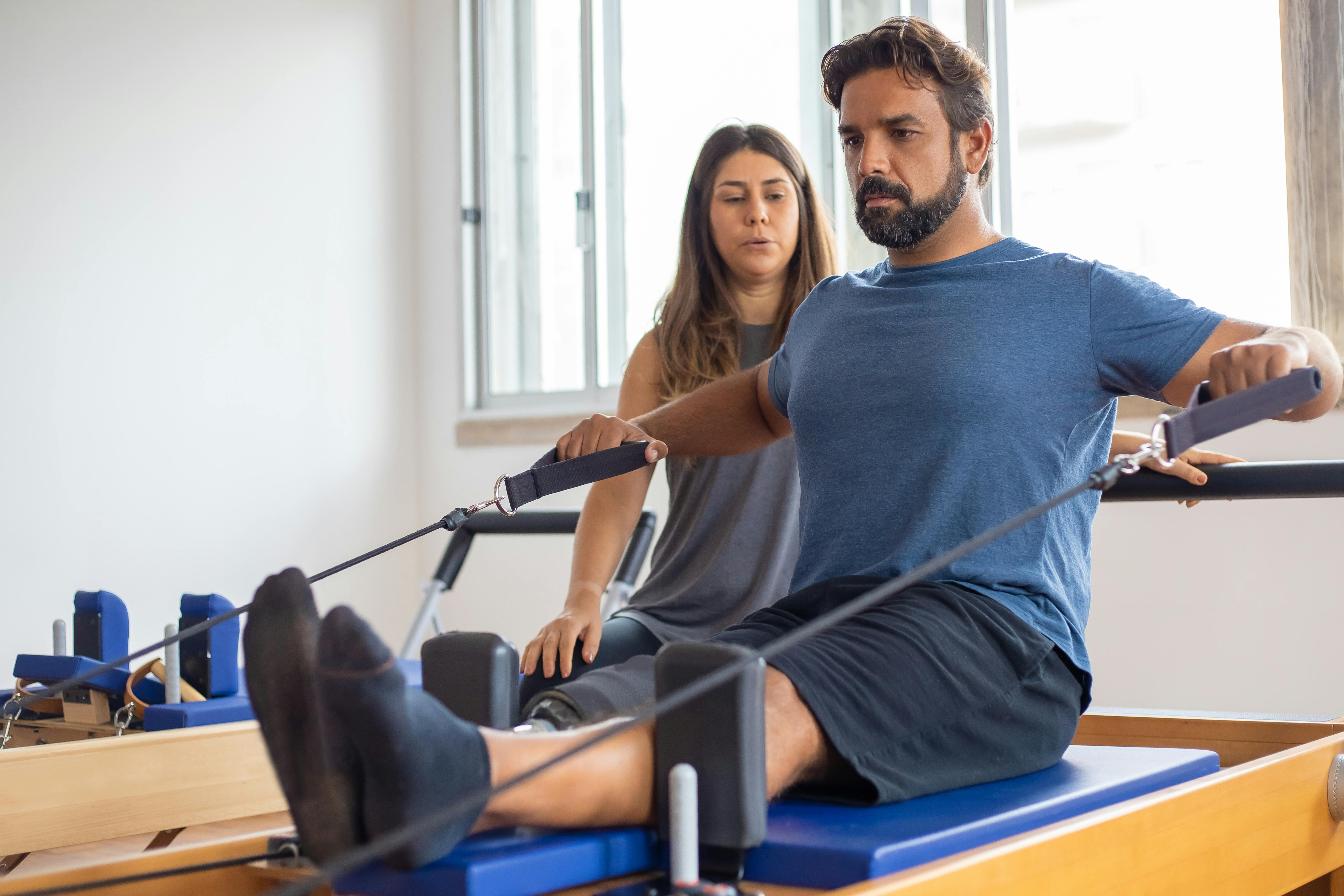 Man stretching with resistance band. A trainer assists from behind.